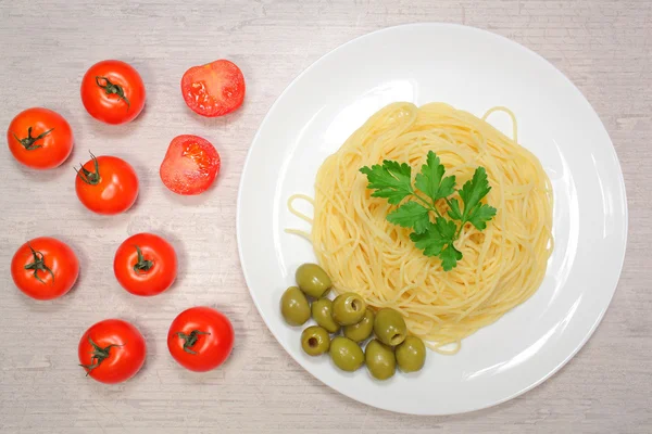 Итальянская еда: макароны на большой белой тарелке рядом с помидорами черри и зелеными оливками — стоковое фото