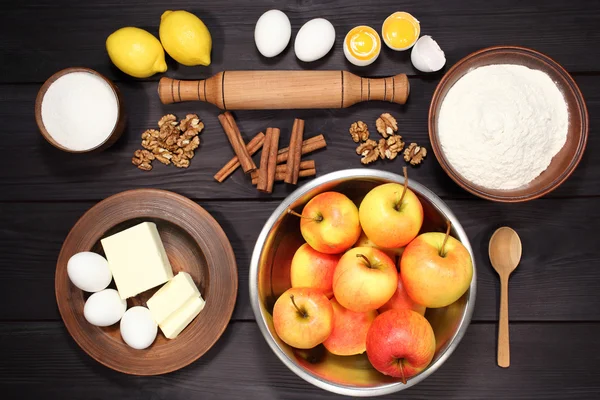 Products and ingredients for making homemade apple pie, spread out on a rustic table in a plates and bowls