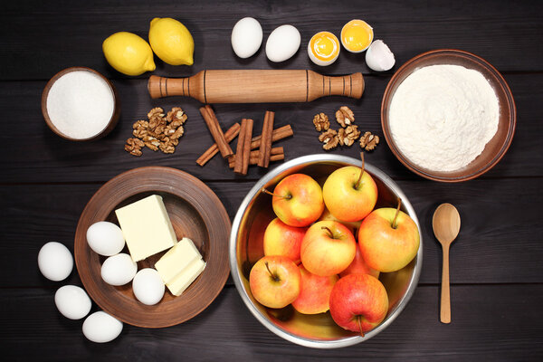 Products and ingredients for making homemade apple pie, spread out on a rustic table in a plates and bowls