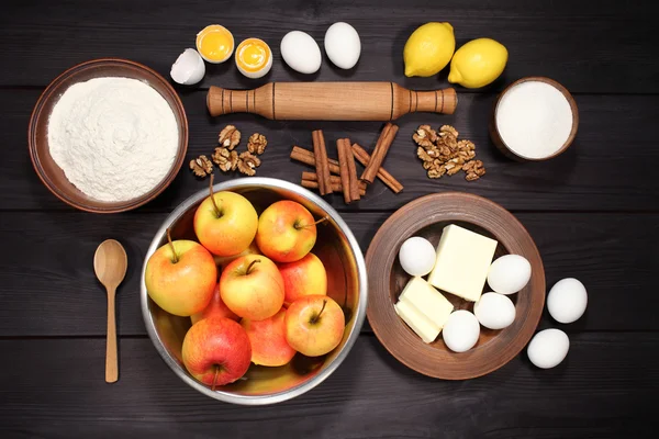 Products and ingredients for making homemade apple pie, spread out on a rustic table in a plates and bowls