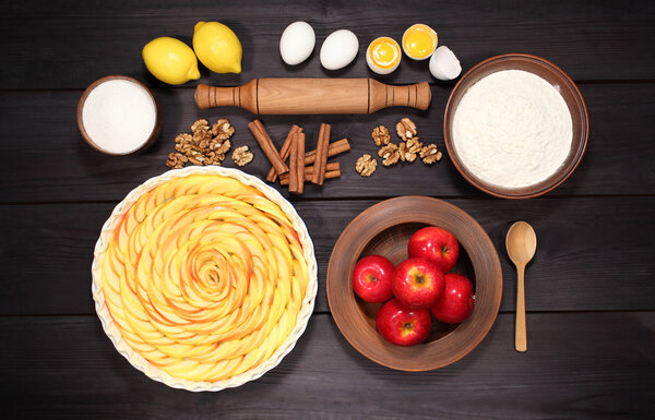 Products and ingredients for making homemade apple pie, spread out on a rustic table in a plates and bowls