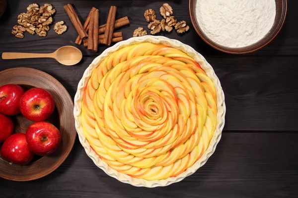 Products and ingredients for making homemade apple pie, spread out on a rustic table in a plates and bowls