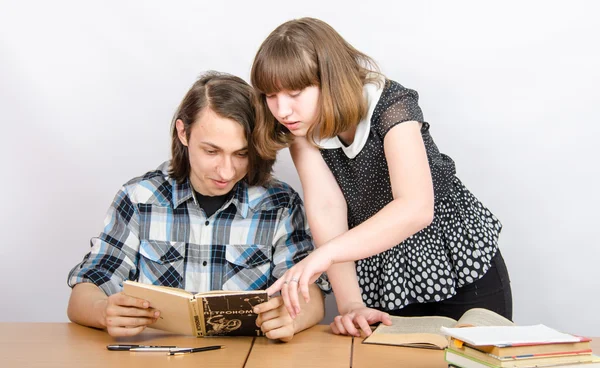 Adolescente olha para um livro que segura a menina — Fotografia de Stock