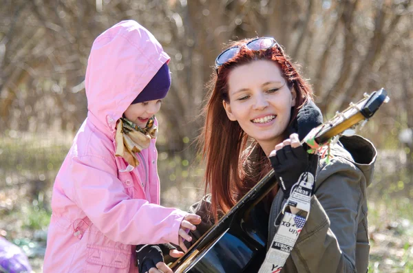 Malá holčička dotykem struny na kytaru, která hraje matku v přírodě — Stock fotografie
