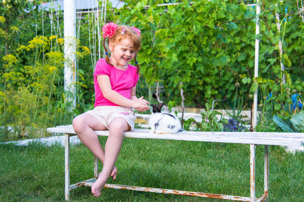 Little girl petting a bunny on a bench in the garden