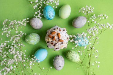 Paskalya. Süslü, çok renkli Paskalya yumurtaları şenlikli pastanın etrafına seriliyor. Yakınlarda beyaz bir çiçek filizleri var..