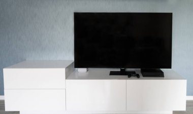 Büyük bir düz ekran televizyon mavi-gri duvarlı bir odada düşük katlı beyaz bir mobilyanın üzerinde oturur..