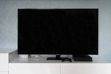 Büyük bir düz ekran televizyon mavi-gri duvarlı bir odada düşük katlı beyaz bir mobilyanın üzerinde oturur..