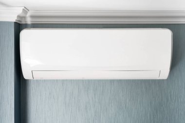 Beyaz bir klima, gri ve mavi duvarlı bir odada beyaz bir tavanın altına kurulur..