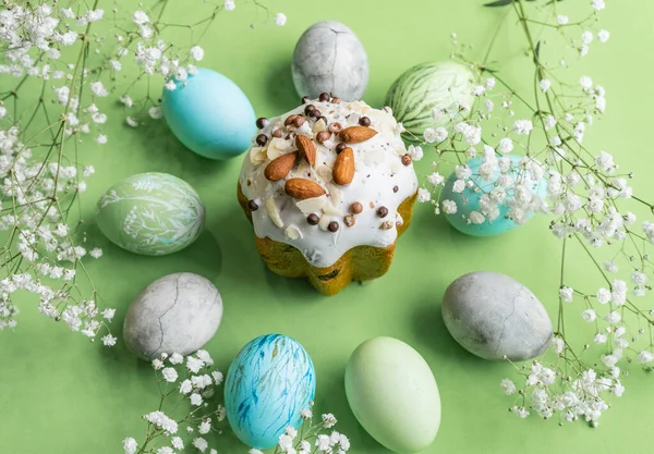 Paskalya. Süslü, çok renkli Paskalya yumurtaları şenlikli pastanın etrafına seriliyor. Yakınlarda beyaz bir çiçek filizleri var..