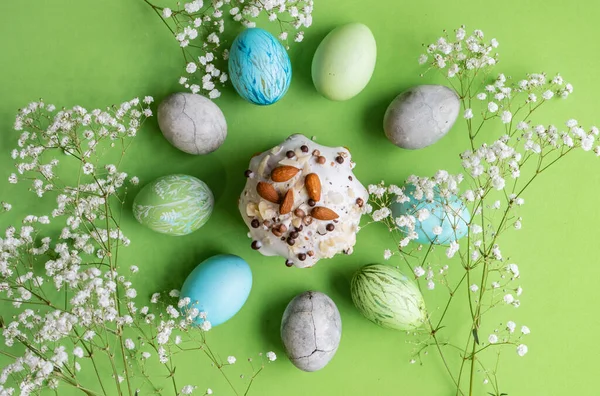 Paskalya. Süslü, çok renkli Paskalya yumurtaları şenlikli pastanın etrafına seriliyor. Yakınlarda beyaz bir çiçek filizleri var..