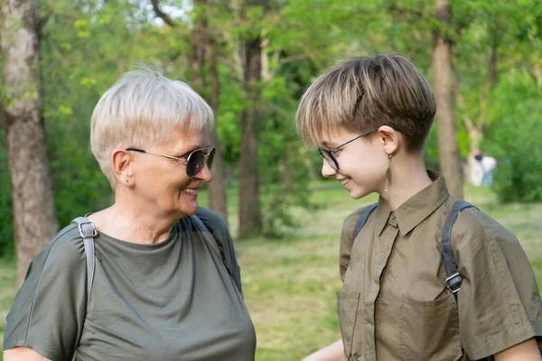Yaşlı, modaya uygun, modern, yaratıcı bir büyükanne ve şık ergen torunu bir yaz parkında gülüyorlar..