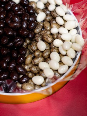 Bir kabın içinde üç çeşit paketlenmemiş şeker: koyu çikolata kaplı fındık, beyaz jöleli fındık ve bıldırcın yumurtası şeklinde fındık..