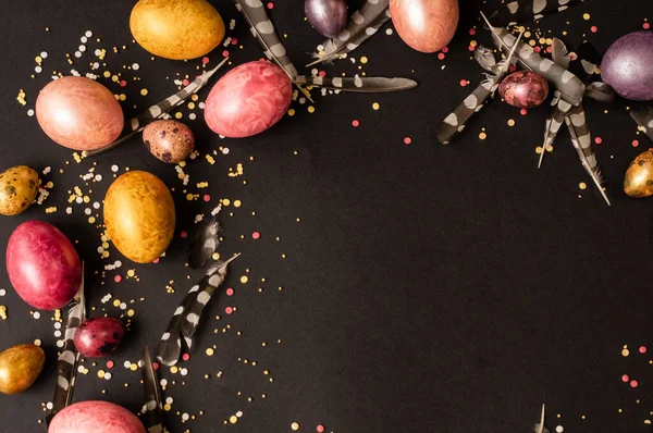 Paskalya tatili. Çok renkli, incilerin anası tavuk ve bıldırcın yumurtaları siyah bir arka planda uzanır, serpiştirilmiş ve tüylerle süslenmiştir..