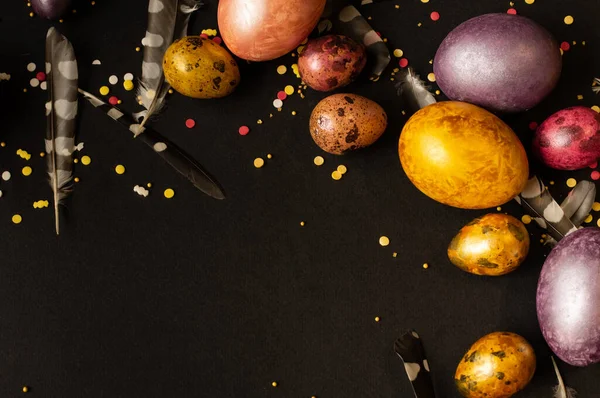 Paskalya tatili. Çok renkli, incilerin anası tavuk ve bıldırcın yumurtaları siyah bir arka planda uzanır, serpiştirilmiş ve tüylerle süslenmiştir..