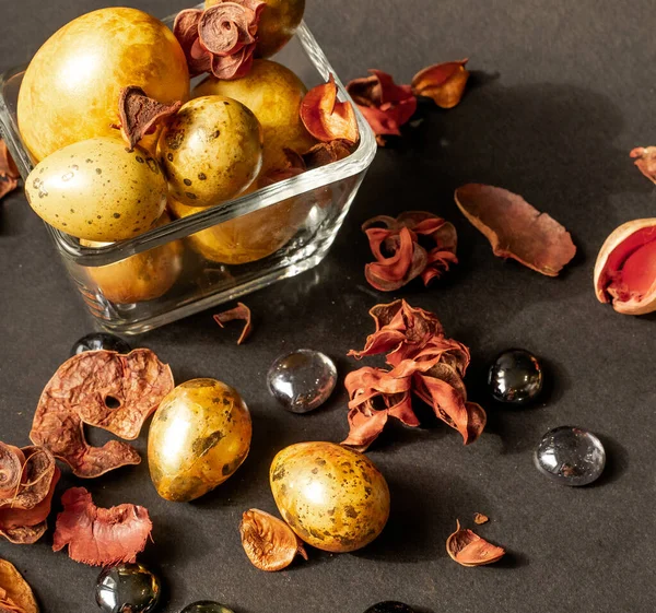 Paskalya tatili. Çok güzel, çeşitli boyutlarda altın yumurtalar küçük cam bir vazoda duruyor. Siyah bir zemin üzerinde. Kurumuş çiçekler ve cam taşlarla süslenmiş..