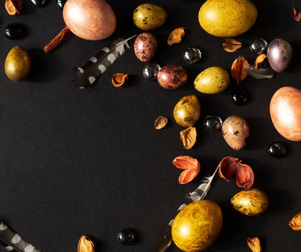 Paskalya. Çok renkli, incilerin anası cam taşlar, kurumuş çiçekler ve tüylerle süslenmiş siyah bir arka planda yatıyor.