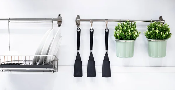 Mutfak duvarında bulaşık ve mutfak aletleri için raflar. Yakınlarda küçük saksılarda süslü çiçekler var..