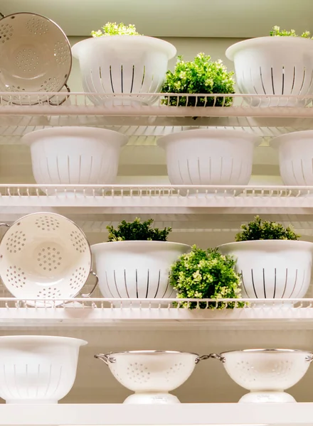 Mağazadaki raflar beyaz ve bej renkli mutfak gereçleri ve çiçeklerle süslenmiştir..