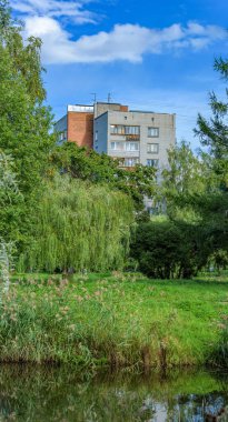 Göletli, sazlıklı, mavi gökyüzünün altında, güneşli bir sonbahar gününde inanılmaz bulutları olan çok katlı binalar..