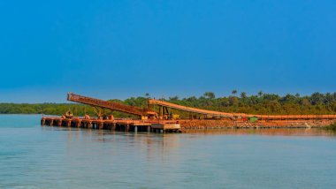 Nehir kıyısındaki açık hava sanayi iskelesi, Bauxite cevheri taşımak için büyük bir taşıyıcı. Maden mekiği trenlerinden, küçük hangar gemilerine (besleyici). Gine, Batı Afrika.