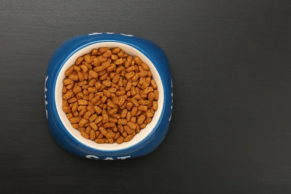Nourriture sèche pour chat dans un bol en céramique sur sol noir — Photo