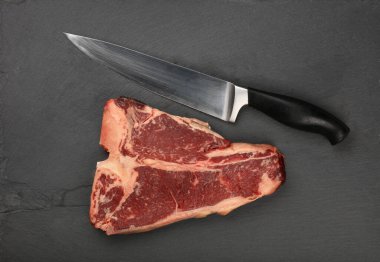 Siyah tahtada kaburga kemikli mermer bifteği kapatıyoruz. Bıçaklı kesme tahtası, üst manzaralı, tam üstte.