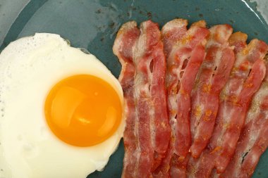 Yakın İngiliz kahvaltısı, güneşli yan yumurta ve kızarmış pastırma dilimleri mavi tabakta, üst manzarada, tam üstte.