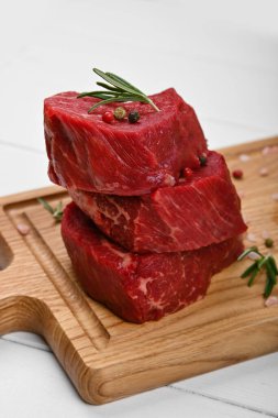 Kazıklı üç adet çiğ fileto ya da fileto fileminyon bifteği kahverengi meşe ağacından kesme tahtasında, baharatlarla, beyaz ahşap masa arka planında, yüksek açılı görüşte.