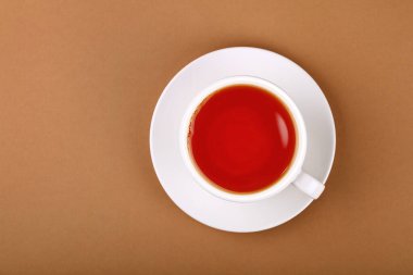 Bir fincan kırmızı siyah ya da meyve çayını kahverengi kağıdın üzerinde, beyaz çay tabağı üzerine koy, üst manzarası tam üstte.
