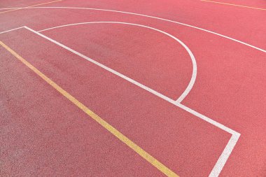 Kırmızı açık hava basketbol sahasının arka planı beyaz ve sarı çizgili, yüksek açılı manzaralı.