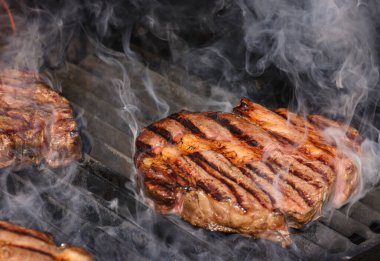 Açık ateşte kavrulmuş, dumanı tüten biftekleri yakın metal ızgaralı, yüksek açılı biftekleri yakın.