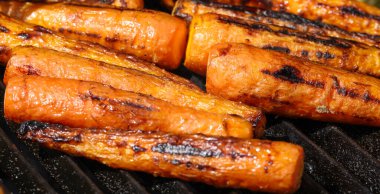 Close up cooking fresh new carrots in outdoor charcoal grill with cast iron metal grate, high angle view