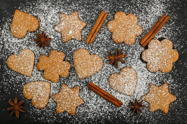 用肉桂和星形茴香调料在黑色石板背景上用粉末状白糖糖霜包裹着心形和星形的圣诞姜饼 高高在上 高高在上 — 图库照片