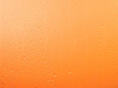 Yağmur damlalarını kapat ve cam pencere yüzeyinde akan su yağmurlu bir günde parlak turuncu günbatımı arka planında.