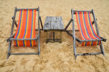 Tayland 'da tatil köyünün kumsalında iki boş renkli kanvas kanvas askı sandalye ve ahşap masa, ön manzara, yüksek açı.