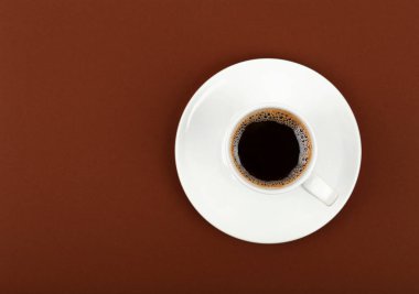 Kahverengi arka planda çay tabağı üzerine sade kahve dolu beyaz bir fincanı kapat. Üst manzarası yüksek, tam üstte.