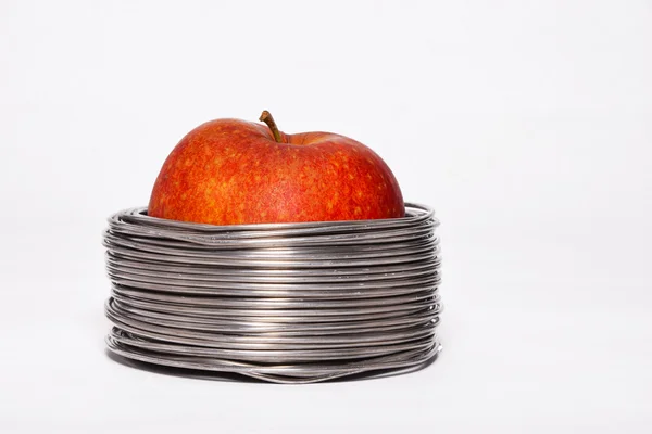 Wired apple: whole red apple in coils of aluminum wire isolated on white background — Stockfoto