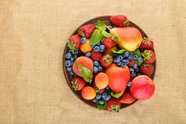 Fruits et baies se mélangent dans une assiette en céramique sur toile de jute — Photo