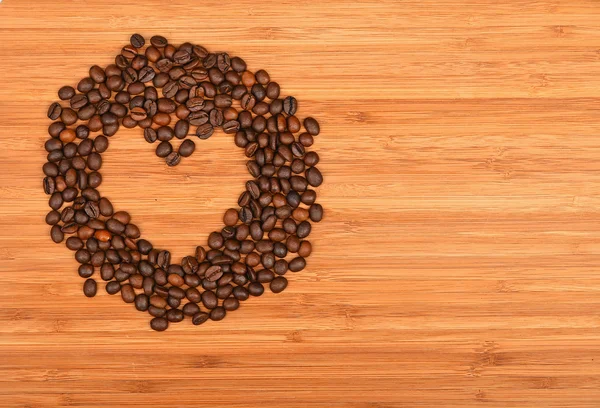 Heart shaped coffee beans frame over bamboo wood background
