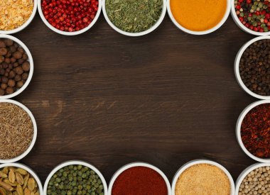 Beyaz seramik kâselerdeki çeşitli baharatların çerçevesi koyu ahşap masa arkaplanının üzerinde fotokopi alanı, yüksek üst manzara, tam üstte.