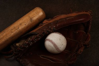 Eski bir beyzbol topunu kapat, ahşap sopa ve eskimiş deri eldiveni grunge koyu kahverengi arka planda, yükseltilmiş üst manzara, tam üstte.