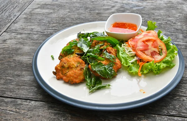 Plate of shrimp cakes with salad on wooden table