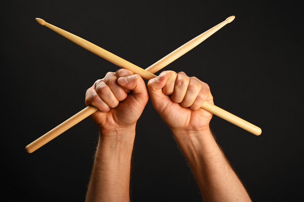 Two hands with crossed drumsticks over black