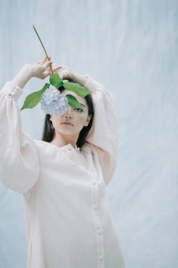 Kumaş arka planda ortanca çiçekleriyle poz veren hassas kadın portresi 