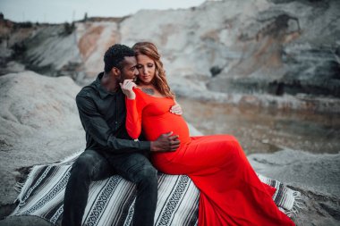  Granit kanyona karşı poz veren çok ırklı bir çift. Şık kırmızı elbise giyen hamile bir kadın. 