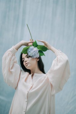 Kumaş arka planda ortanca çiçekleriyle poz veren hassas kadın portresi 