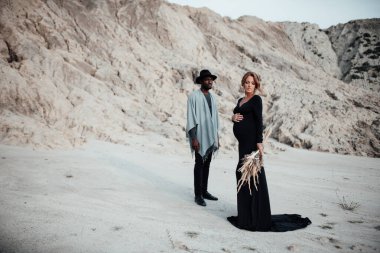 Granit kanyona karşı poz veren çok ırklı bir çift. Siyah bir elbise giyen hamile bir kadın. 