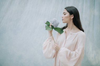 Kumaş arka planda ortanca çiçekleriyle poz veren hassas kadın portresi 