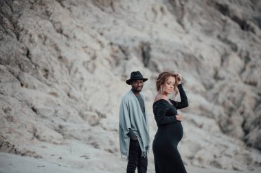 Granit kanyona karşı poz veren çok ırklı bir çift. Siyah bir elbise giyen hamile bir kadın. 